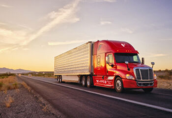 red semi-truck driving on a road during sunset