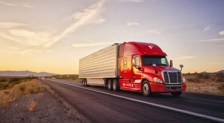 red semi-truck driving on a road during sunset