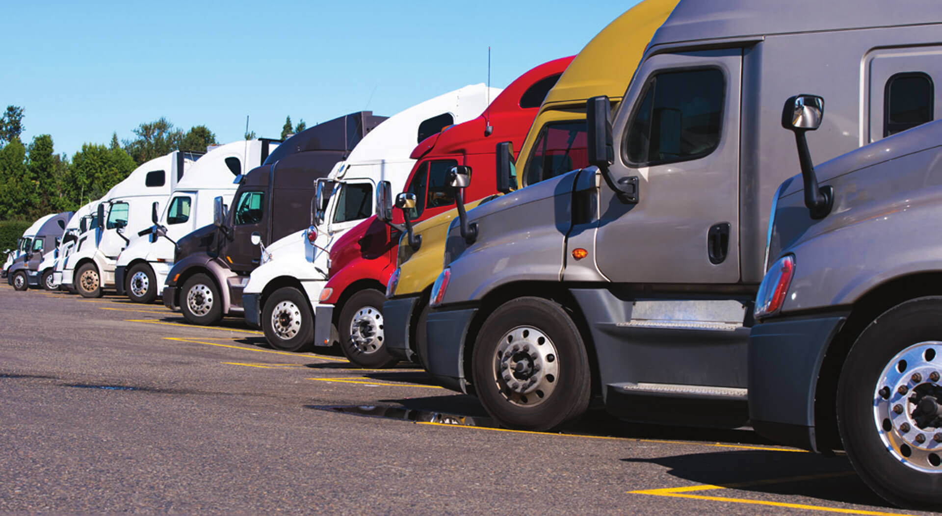 big rigs semi trucks of different colors, makes, and models stand in row on truck stop parking lot